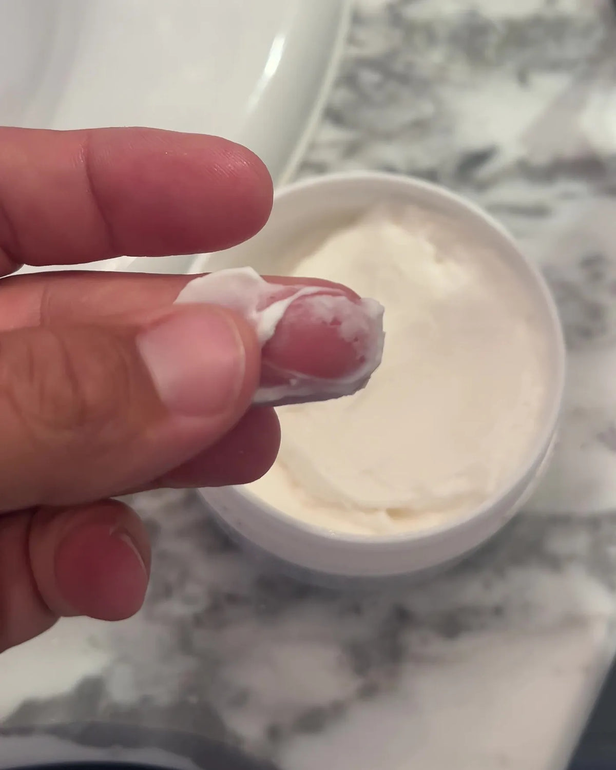 Fingertip with a scoop of cream above an open jar