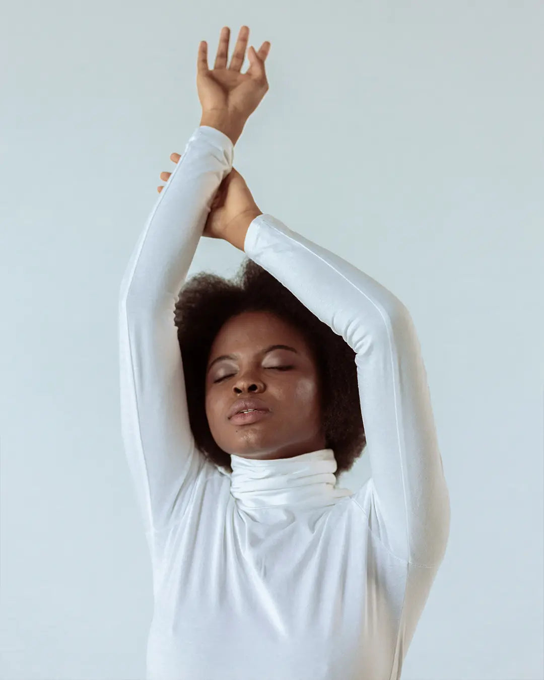 Woman in a white turtleneck stretching her arms overhead
